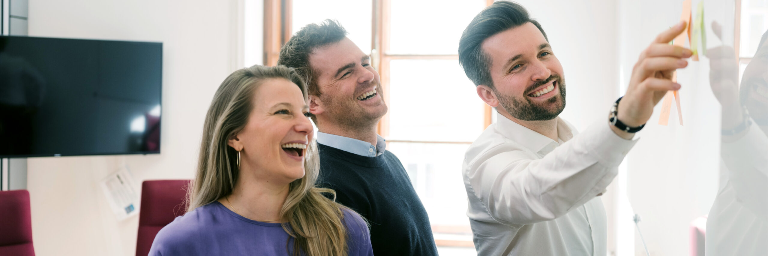 Auf diesem Foto sind Irene Racher, Stefan Pachernegg und Oliver Bandyk zu sehen, die an einem Whiteboard arbeiten und lächeln.