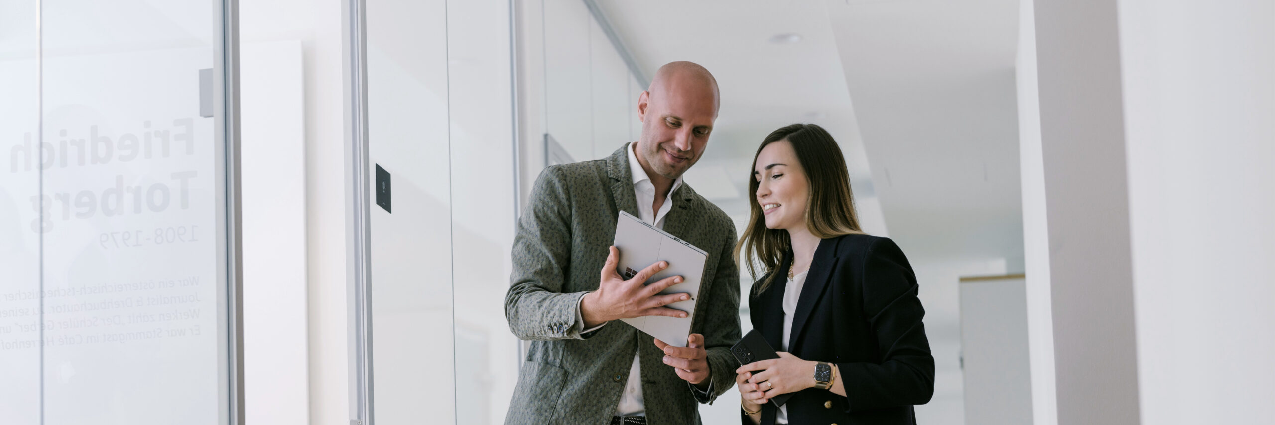 Auf diesem Bild sind links ein männlicher Consultant mit einem Tablet in der Hand und rechts ein weiblicher consultant, der in das Tablet schaut zu sehen.