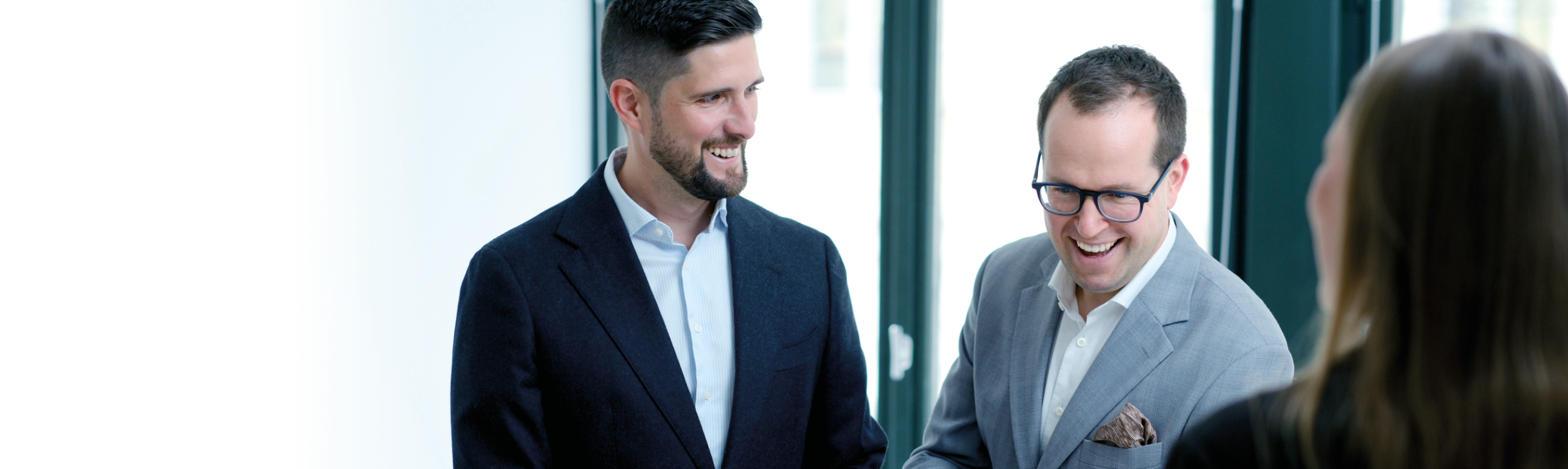 Michael Rinda is smiling at another consultant, who is looking down, also smiling. On the right corner is a women from the back.