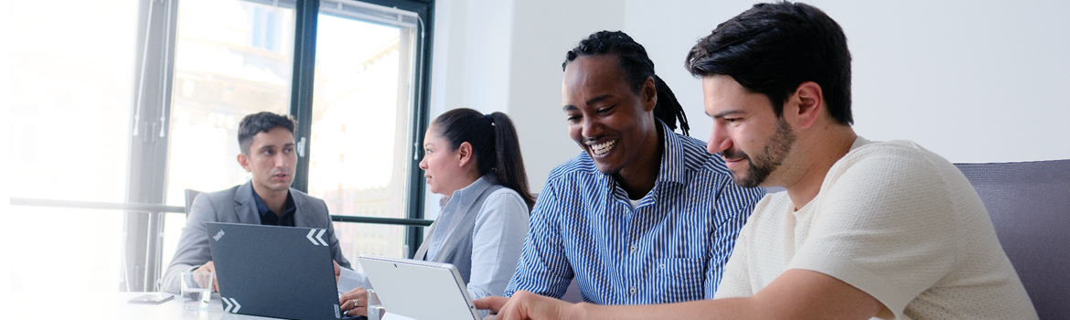 Four consultants are working together in a bright office, engaged in discussion and using laptops.