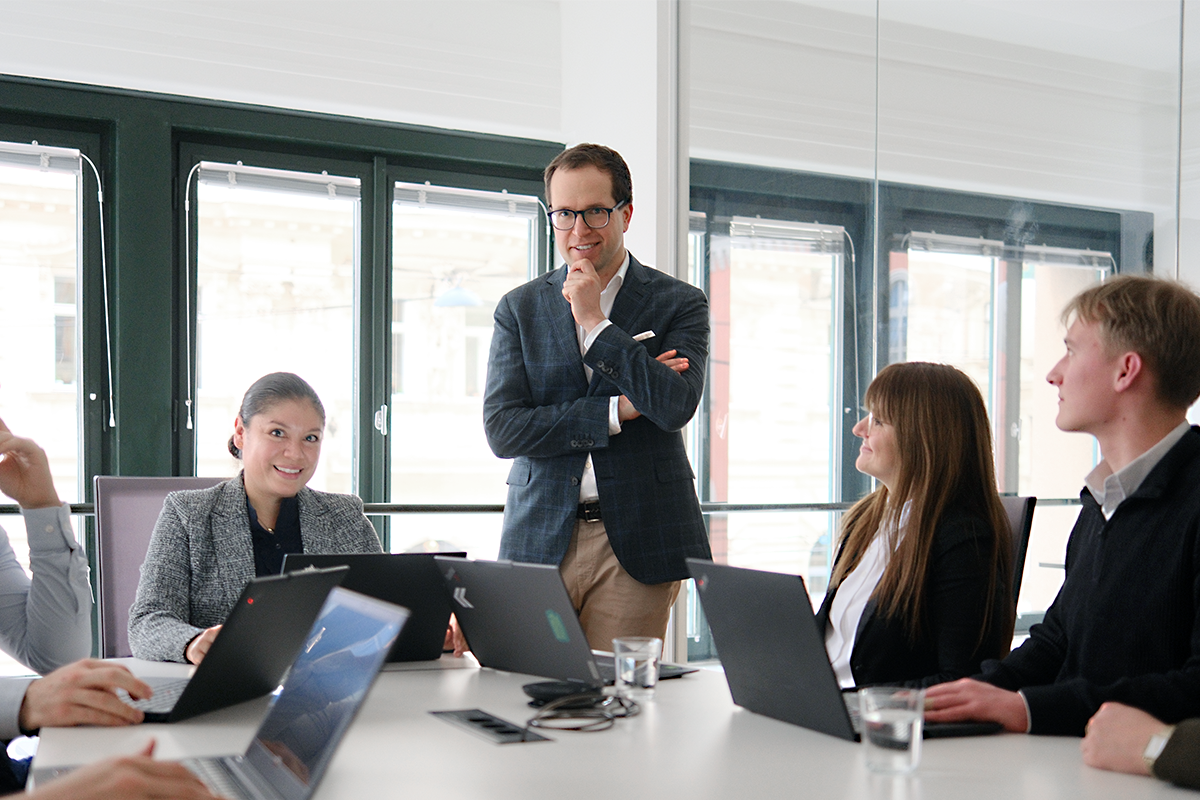 Aan Szwajkowski im Fokus stehend am Tisch und Team Compliance rund um den Tisch im EFS Office.